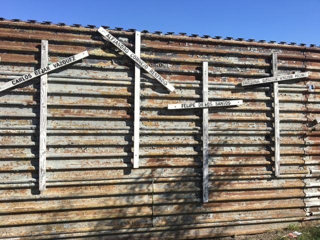 Image of the Mexico/US borderwall with crosses on it and names of those who have died.
